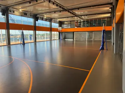 Die leere Sporthalle an Bord der MSC Euribia mit Toren, Basketballkorb und großem Fenster mit Blick auf den Hafen.