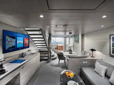 Ein moderner, heller Wohnbereich einer Duplex Suite an Bord der MSC Euribia. Zu sehen sind Sofa, Esstisch, Kaffeemaschine, großer TV, eine Treppe und ein Balkon mit Whirlpool.