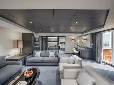 MSC Euribia: Moderne MSC Yacht Club Royal Suite. Eleganter Wohnbereich mit Sofas, Schreibtisch, Balkon mit Meerblick und Whirlpool. Hinten: Schlafzimmer.