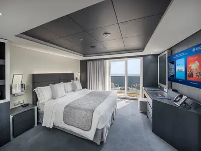 Eine stilvolle Suite an Bord der MSC Euribia mit Doppelbett, Nachttischen, Schreibtisch mit TV und privatem Balkon. Moderne Eleganz in Grau- und Weisstönen mit Meerblick.