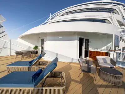 Private Terrasse der Royal Suite an Bord der MSC Euribia. Holzdeck, Liegen, Essbereich, Lounge-Sessel, Whirlpool. Moderne Architektur, blauer Himmel.