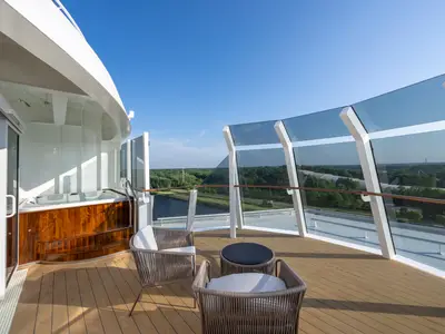 Geräumige private Terrasse einer Royal Suite an Bord der MSC Euribia. Ein Whirlpool und moderne Lounge-Möbel bieten Komfort. Eine Glasbrüstung gibt den weiten Blick auf eine grüne Landschaft frei.