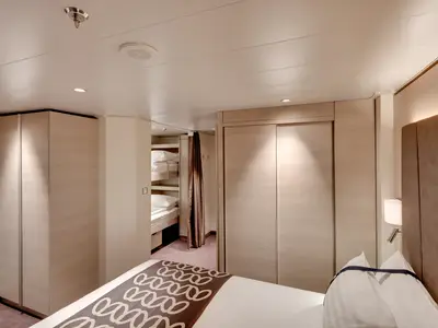 Moderne Suite an Bord der MSC Euribia, ausgestattet mit Doppelbett und Etagenbetten. Helle Holzmöbel und indirekte Beleuchtung prägen das gemütliche Ambiente für Familien.
