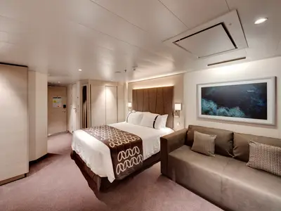 Eine luxuriöse Premium Suite Aurea an Bord der MSC Euribia. Sie zeigt ein gemütliches Doppelbett, eine bequeme Couch und elegante Einbauschränke in warmen Farbtönen.