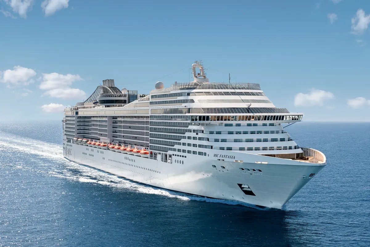 Die MSC Fantasia gleitet auf dem offenen Meer unter strahlend blauem Himmel. Das weiße Kreuzfahrtschiff ist von oben fotografiert und erzeugt eine Schaumspur im tiefblauen Wasser.