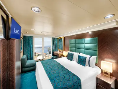 Innenansicht einer geräumigen Balkonkabine an Bord der MSC Fantasia mit Doppelbett, Sitzbereich, Flachbildfernseher und Blick auf das Meer vom Balkon.