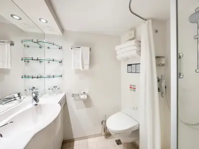 Helles, modernes Badezimmer in einer Deluxe Balkonkabine der MSC Fantasia mit Waschbecken, Toilette und Duschbereich. Weiße Wände, Chromarmaturen und frische Handtücher sind zu sehen.