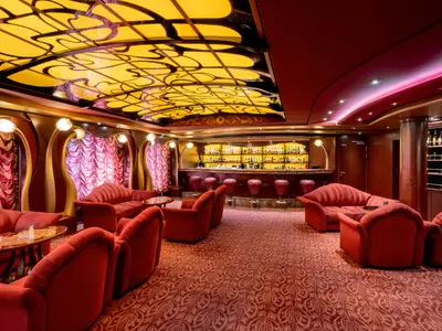 Innenansicht der roten Bar-Lounge an Bord der MSC Fantasia mit beleuchteter Bar, Samtsofas, Sesseln und kunstvoller goldener Decke.