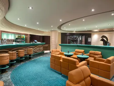 Die Fantasia Bar an Bord der MSC Fantasia, mit einer langen, geschwungenen Bar, braunen Barhockern und mehreren orangefarbenen Sesseln und Tischen im Lounge-Bereich.