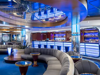 Blick in die stilvolle Il Transatlantico Bar-Lounge an Bord der MSC Fantasia mit geschwungenen Sofas, beleuchteter Bar und blauer Raumbeleuchtung.