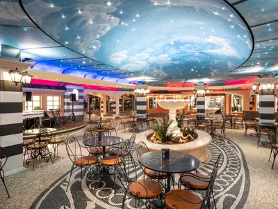 Bar-Lounge, Piazza San Giorgio, an Bord der MSC Fantasia. Zahlreiche Tische und Stühle umrahmen einen zentralen Brunnen. Die Decke ist als kunstvoller Sternenhimmel mit Wolken gestaltet.