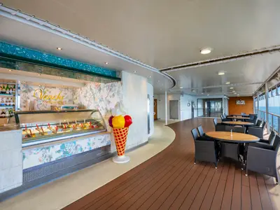 Überdachte Venchi Gelateria auf der MSC Fantasia. Eisstand, bunte Eisskulptur, elegante Tische und Stühle mit weitem Meerblick.