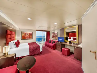 Eine geräumige, elegant eingerichtete Balkonkabine an Bord der MSC Fantasia. Sie verfügt über ein Doppelbett, ein rotes Sofa, einen Schreibtisch mit TV und einen Balkon mit Meerblick.