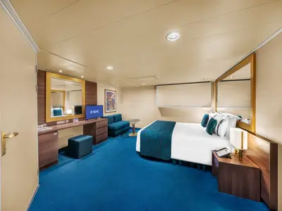 Blick in eine geraeumige barrierefreie Innenkabine an Bord der MSC Fantasia. Die Kabine verfuegt ueber ein Doppelbett, eine Sitzecke mit Sofa und Couchtisch sowie einen Schreibtisch mit TV und Minibar. Der Boden ist mit blauem Teppich ausgelegt. Eine harmonische und komfortable Unterkunft.
