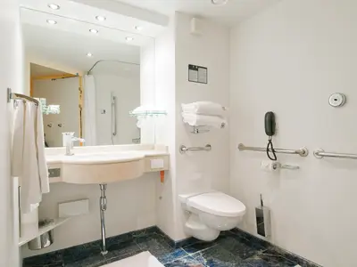 Helles, barrierefreies Badezimmer an Bord der MSC Fantasia mit WC, Waschbecken, Haltegriffen und Notruftelefon. Das Design ist modern und praktisch.