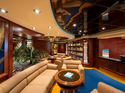 Ein eleganter Innenraum der MSC Fantasia mit einer Bibliothek, braunen Holzvertäfelungen, beigen Sofas und Stühlen, einem reflektierenden Deckenbereich und einem Concierge-Schalter.