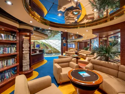 Elegante Bibliothek und Lounge an Bord der MSC Fantasia. Sichtbar sind Bücherregale, Sitzgruppen, Tische, Pflanzen und eine Rezeption unter einer kunstvollen Decke.