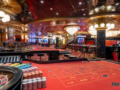 Das opulente Casino Delle Palme an Bord der MSC Fantasia. Ein roter Roulette-Tisch mit Chips im Vordergrund. Weitere Spielautomaten und eine Bar sind im luxuriösen Ambiente sichtbar.