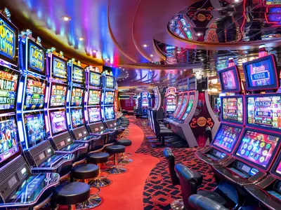 Blick auf das Casino Delle Palme an Bord der MSC Fantasia. Zahlreiche leuchtende Slot-Maschinen, roter Teppich und reflektierende Decke schaffen eine lebhafte Atmosphäre mit bunter Beleuchtung.
