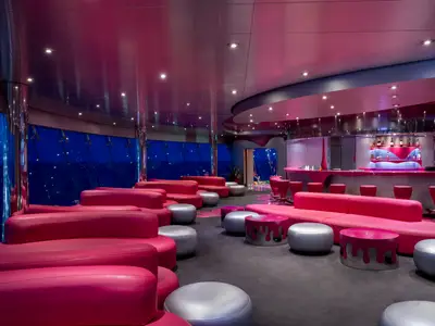 Die futuristische Liquid Disco an Bord der MSC Fantasia. Der Raum ist mit pinken Sofas, Hockern und einer beleuchteten Bar ausgestattet. Große Fenster zeigen das dunkle Meer. Eine moderne und lebhafte Atmosphäre.