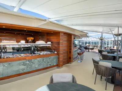 Ueberdachtes Outdoor-Buffet auf der MSC Fantasia mit einer Bar und Lounge-Sitzbereichen. Links das Buffet, rechts moderne Tische und Stuehle.