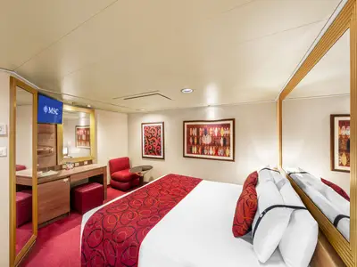 Eine helle und gemuetliche Innenkabine an Bord der MSC Fantasia. Zu sehen sind ein Doppelbett, ein roter Sessel, ein Schminktisch mit Hocker, Kunstwerke und ein TV mit MSC Logo.