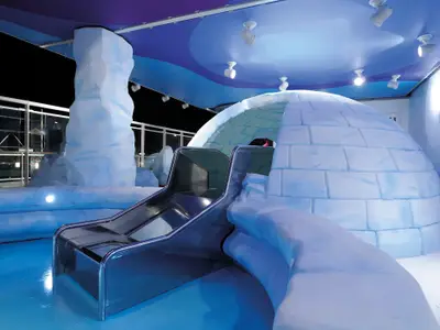 Kinderbereich 'Il Polo Nord' auf der MSC Fantasia mit Rutsche, Iglo und Eisskulpturen in arktischem Design. Blaues Licht schafft eine winterliche Atmosphäre, keine Personen sichtbar.
