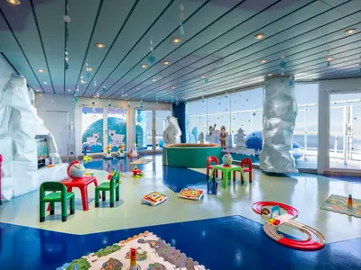 Heller, arktisch thematisierter Kinderbereich 'Polo Nord' an Bord der MSC Fantasia. Mit Eisberg-Deko, großem Polar-Bären, Kindermöbeln und Spielzeug auf dem bunten Boden. Große Fenster bieten Meerblick.