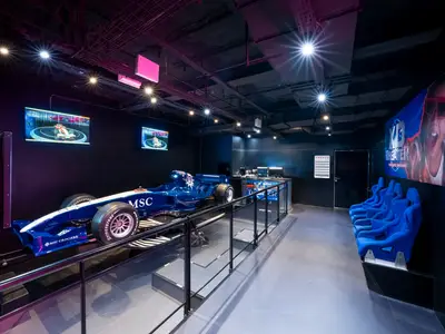 Ein futuristischer Bereich an Bord der MSC Fantasia mit einem blauen Formel-Rennsimulator, großen Bildschirmen und blauen Sitzen für ein XD Theater. Die Decke ist schwarz, beleuchtet von Strahlern.