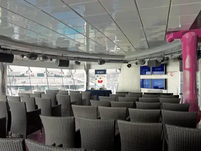 Blick in einen Konferenzraum an Bord der MSC Fantasia mit vielen grauen Korbsesseln, Tischen, Bildschirmen und Fenstern mit Aussicht auf den Hafen.