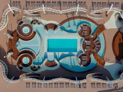 Vogelperspektive auf den weitläufigen Aqua Park an Bord der MSC Fantasia mit mehreren Pools, Whirlpools und vielen Liegeflächen auf dem sonnigen Holzdeck.