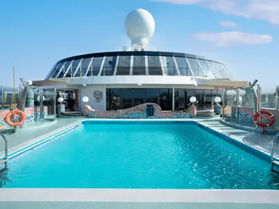 Der Poolbereich Lido Catalano der MSC Fantasia mit blauem Wasser. Ein verglastes Gebäude mit Kuppeldach ist im Hintergrund zu sehen. Rettungsringe sind sichtbar.