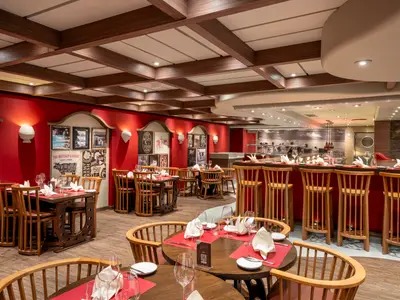 Blick ins Spezialitätenrestaurant Butcher's Cut der MSC Fantasia. Rote Wände mit Bildern, Holztische, Stühle und eine Bar. Hell beleuchtet, ohne Personen.