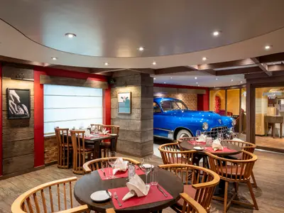 Das elegant eingerichtete Spezialitätenrestaurant Butcher's Cut an Bord der MSC Fantasia mit dunklen Holztischen und Stühlen. Im Hintergrund ein glänzender blauer Oldtimer.
