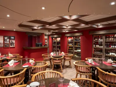 Innenansicht des Spezialitätenrestaurants Butcher's Cut an Bord der MSC Fantasia mit roten Wänden, Holztischen und Stühlen. Beleuchtete Weinregale im Hintergrund.