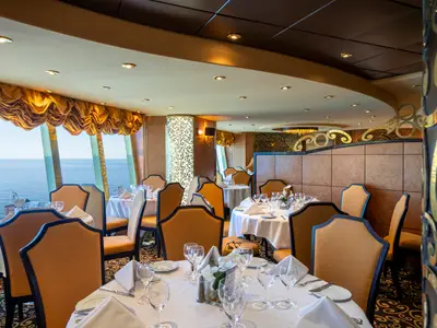 Blick in das elegante Restaurant Il Cerchio D'Oro an Bord der MSC Fantasia. Zahlreiche Tische sind mit weißen Tischdecken, Besteck, Gläsern und Blumen dekoriert. Große Fenster bieten einen weiten Blick auf das offene Meer.