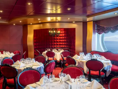 Restaurant 'Red Velvet' an Bord der MSC Fantasia mit roten Samtstühlen und festlich gedeckten Tischen. Warme Beleuchtung und Bullauge mit Meerblick schaffen eine elegante Atmosphäre.
