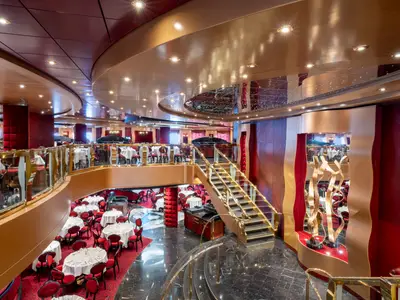 Zweistöckiges Red Velvet Restaurant an Bord der MSC Fantasia. Elegante Tische, rote Stühle, goldene Geländer und eine Treppe prägen das opulente Ambiente.