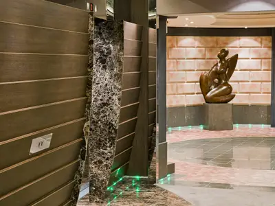 Atrium an Bord der MSC Fantasia mit einer großen sitzenden Bronze-Skulptur und modernem Design aus Holz, Marmor und beleuchteten Bodenelementen.