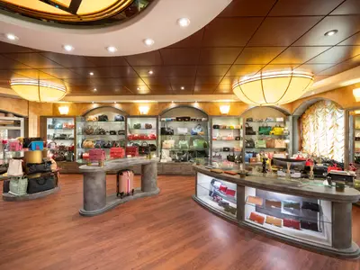 Elegante Boutique an Bord der MSC Fantasia, mit vielen Designer-Handtaschen und Gepäck in Glasvitrinen und auf Podesten. Der Raum hat Holzboden und große Deckenleuchten.