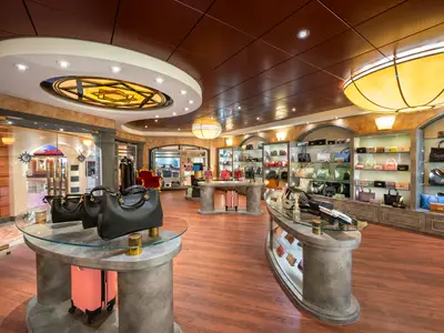 Luxuriöser Accessoires-Shop an Bord der MSC Fantasia. Schwarze Handtaschen auf Glastischen, farbige Taschen in beleuchteten Vitrinen. Elegante, warm beleuchtete Einrichtung.