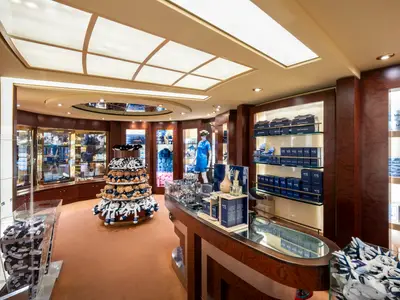 Blick in den gut beleuchteten Logo Shop an Bord der MSC Fantasia. Praesentiert werden Souvenirs, Kleidung, Parfum und Plueschtiere in Holzregalen.