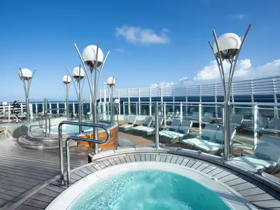 Blick auf das obere Sonnendeck der MSC Fantasia mit mehreren runden Whirlpools, Holzdecks und vielen leeren Sonnenliegen unter blauem Himmel mit leichten Wolken.