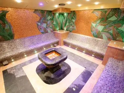 Detailansicht des luxuriösen Dampfbads im MSC Aurea Spa an Bord der MSC Fantasia. Mosaikverzierte Wände, bequeme Sitzbänke und ein zentrales Wasserelement mit indirekter Beleuchtung.