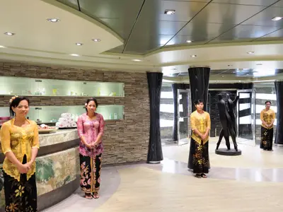 Vier weibliche Crew-Mitglieder in traditionellen, farbenfrohen Kleidern stehen an der Rezeption des modernen MSC Aurea Spa an Bord der MSC Fantasia. Im Hintergrund Regale mit Produkten.