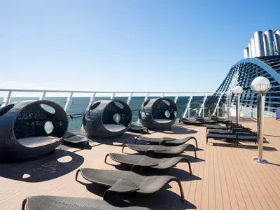 Exklusives Sonnendeck der MSC Fantasia bei Tag, mit stilvollen Lounge-Kojen, Sonnenliegen und Blick auf das weite Meer und den Schornstein des Schiffes.