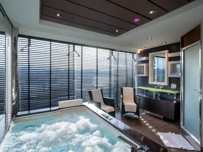 Spa-Bereich an Bord der MSC Fantasia mit sprudelndem Whirlpool, Sesseln, Waschtisch und Spiegel. Große Fenster mit Jalousien lassen Tageslicht ein.