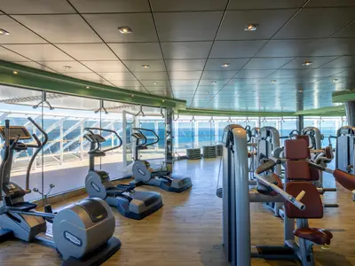 Innenansicht des modernen Fitnessstudios an Bord der MSC Fantasia. Zahlreiche Technogym-Geräte stehen bereit, mit großen Panoramafenstern zum Meer.