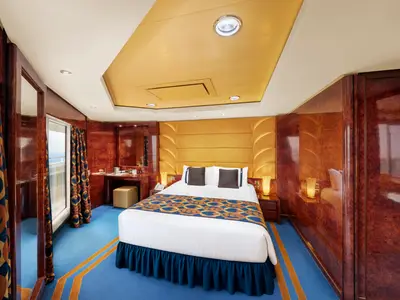 Geräumige Grand Suite Aurea an Bord der MSC Fantasia. Ein luxuriöses Doppelbett, holzvertäfelte Wände, ein Schminktisch und ein Balkonfenster mit Meerblick prägen die elegante Kabine.