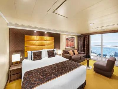 Geräumige Premium Suite Aurea an Bord der MSC Fantasia. Im Vordergrund ein Bett, gefolgt von einer Sitzecke mit Sofa und Sessel. Im Hintergrund ist ein Balkon mit Meerblick zu sehen.